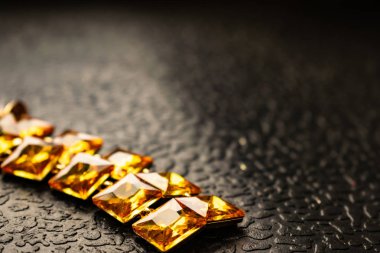 Güzel ve şık takı ve kadınlar için aksesuar. Karanlık ve ahşap dokulu arka plan üzerinde kare taşlarla sarı, turuncu taşlar. Hardal parlak rhinestones altın metal altlığı. İlginç şekil küçük çakıl taşları.