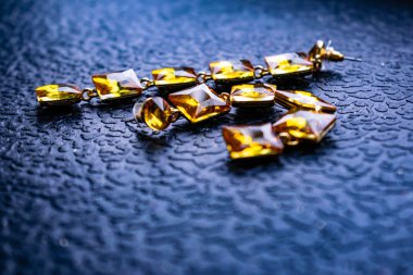 Güzel ve şık takı ve kadınlar için aksesuar. Karanlık ve ahşap dokulu arka plan üzerinde kare taşlarla sarı, turuncu taşlar. Hardal parlak rhinestones altın metal altlığı. İlginç şekil küçük çakıl taşları.