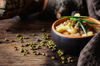 Püre ve patatesli çorba. Kavanozdan yeşil soğan ve bezelye ile süslenmiş. Kömürleşmiş ahşap bir arka planda, kumaş ve doğal dallarla seramik bir tencerede servis yapmak.