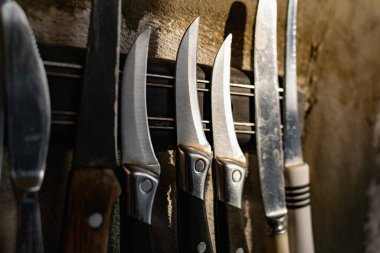 Yatay mıknatıs tutacağında asılı farklı boyutlarda ve şekillerde metal bıçaklar. Blok ve çimentodan yapılmış gri beton bir duvarda