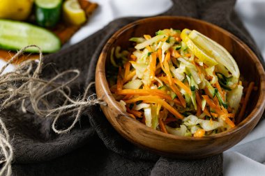 Derin bir tabakta taze sebzelerden oluşan sağlıklı bir salata. Beyaz lahana, havuç ve limon dilimleri ve otlarla süslenmiş mis kokulu salatalıkla dolu bir tabak. Sağlıklı beslenmenin ilginç bir sunumu