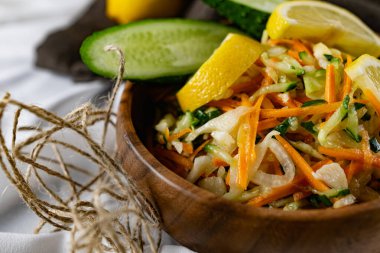 Derin bir tabakta taze sebzelerden oluşan sağlıklı bir salata. Beyaz lahana, havuç ve limon dilimleri ve otlarla süslenmiş mis kokulu salatalıkla dolu bir tabak. Sağlıklı beslenmenin ilginç bir sunumu