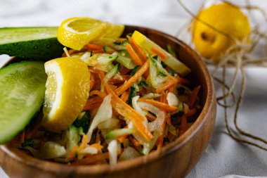 Derin bir tabakta taze sebzelerden oluşan sağlıklı bir salata. Beyaz lahana, havuç ve limon dilimleri ve otlarla süslenmiş mis kokulu salatalıkla dolu bir tabak. Sağlıklı beslenmenin ilginç bir sunumu