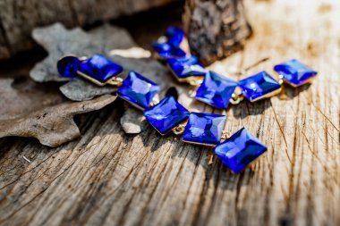 Bayram günü için kostüm mücevherleri, büyük kare mavi taşlı uzun küpeler ve ultra deniz bileziği. Doğal elementlerin kuru ahşap yüzeyinde zarif aksesuarlar.