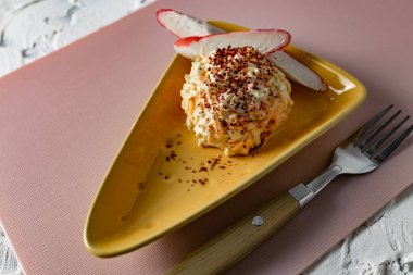 Yengeç salatasını havuç ve peynirle servis etmek, ilginç bir tabakta kurutulmuş nar serpiştirmek, delikleri olan üçgen peynirli, yumuşak pembe arka planda yengeç eti dilimleriyle.