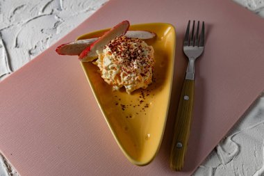 Yengeç salatasını havuç ve peynirle servis etmek, ilginç bir tabakta kurutulmuş nar serpiştirmek, delikleri olan üçgen peynirli, yumuşak pembe arka planda yengeç eti dilimleriyle.