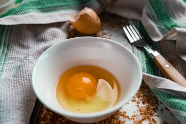 Çiğ yumurta yumurta yumurta, yumurta sarısı ve protein ile beyaz bir kaseye, kabuğun yanında, paslı metal bir arka planda çatal ve havlu, köyde olduğu gibi, basit ve sıradan her şey 
