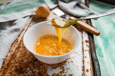 Çatal ve çiğ yumurtayla çırpılmış yumurta, yumurta sarısı ve protein ile beyaz bir kaseye bölünmüş, kabuğun yanında, paslı metal bir arka planda çatal ve havlu, köydeki her şey basit ve sıradan.