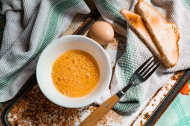 Çatal ve çiğ yumurtayla çırpılmış yumurta, yumurta sarısı ve protein ile beyaz bir kaseye bölünmüş, kabuğun yanında, paslı metal bir arka planda çatal ve havlu, köydeki her şey basit ve sıradan.