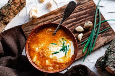 Kahverengi bir tabakta kırmızı borş, eski bir tahta tahtanın yanında sarımsak ve bıldırcın yumurtası, yeşil pırasa ve süzülen dallar. Çorbada beyaz ekşi krema, eski bir Polonya kaşığının yanında.