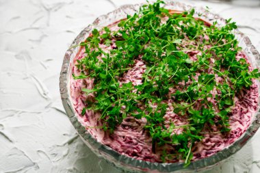 Kürk mantonun altında şişirilmiş salata ringası olan büyük kristal bir cam kase, haşlanmış pancar ve mayonez ile dolu bir Rus yemeği, üstünde yeşil su teresi yaprakları. Beyaz desenli taş zemin