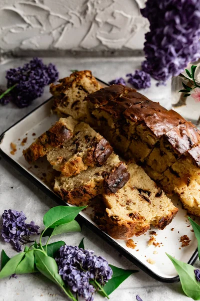 A large pie, cut into portions, stuffed with fruit and berries, among the branches of purple lilac blooming in spring. Homemade cakes on a tea tray.