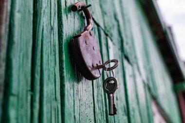 Eski ahır kilitleri ve anahtarlar boyanmış yeşil ahşap duvarda asılı. Kapıları kapatmak için paslı metal aygıt.