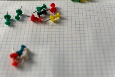 Colored small office buttons with different convenient protective hats, modern office details scattered on notebook leaves in a check