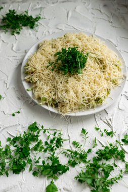 Katmanlı salata, rendelenmiş sert peynirli, marul yapraklı, su teresi yeşili ve beyaz, beton bir arka planda desenli.