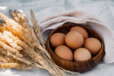 Koyu ahşap bir tabakta tavuk yumurtaları, altın kulaklı kuru dalların ve sade süt ürünlerinin yanında daire içine serilir.