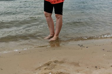 Islak kumlu sahilde çıplak ayaklı kadınlar. Yaz, tatlı su plajı. Nehir kıyısında yürü, bacaklarını yaklaştır..