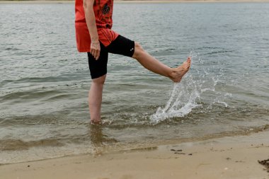 Islak kumlu sahilde çıplak ayaklı kadınlar. Yaz, tatlı su plajı. Nehir kıyısında yürü, bacaklarını yaklaştır..