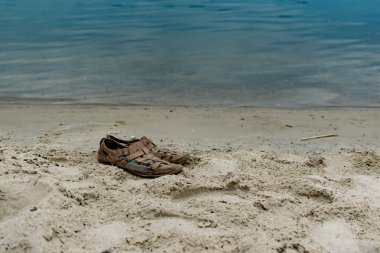 Eski kahverengi ayakkabılar, kumlu sahilde tek başına durmak. Denetimsiz bir şekilde erkek ayakkabılarını çiğnedi.