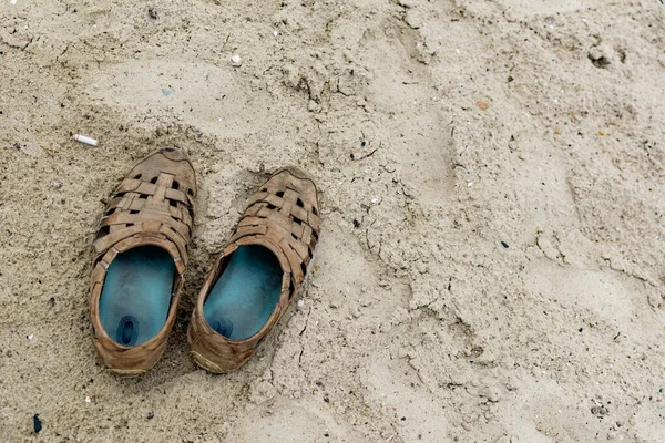Eski kahverengi ayakkabılar, kumlu sahilde tek başına durmak. Denetimsiz bir şekilde erkek ayakkabılarını çiğnedi.