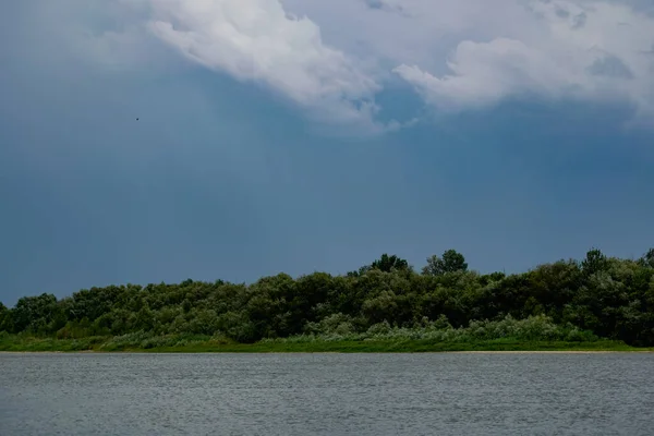 Simple landscape with the freshwater river don in the Rostov region. Warm season, summer, cloudy sky over the sandy beach and green vegetation.