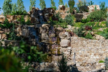 Küçük yapay bir tatlı su şelalesi yaygın bir yaşayan gölete akar. Yeşil yosun ve bitki örtülü arsa yapısı. Doğal elementlerin ve detayların güzel tasarımı.