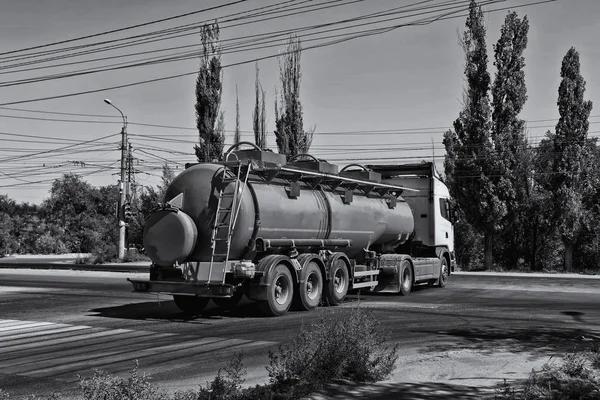 A truck with a tank for transportation of petroleum products traveling on a dusty road at an industrial area