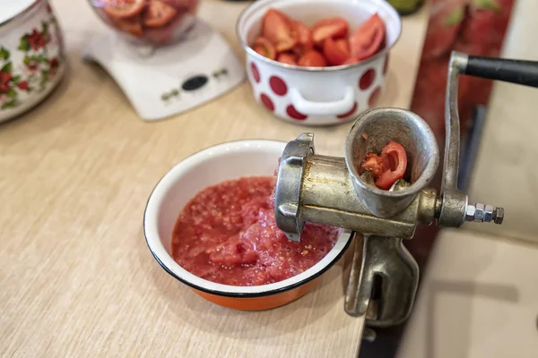 Twist tomatoes into tomato puree with an old hand grinder. Preparation of canned vegetables at home