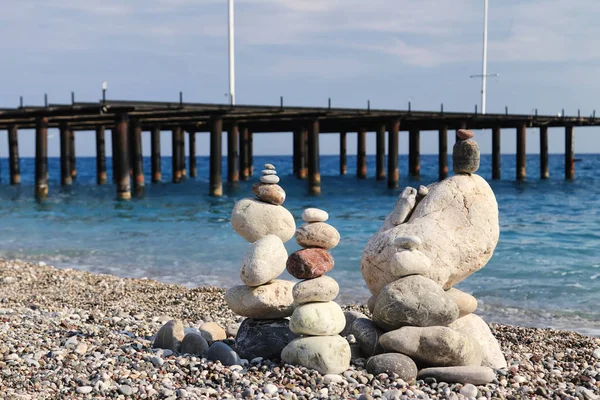 Sea stones of different sizes are built in a pyramid and keep balance. Coastal shoreline with views of the sea and pebble beach