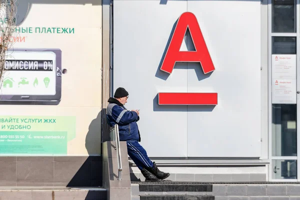 En äldre man står mellan grenarna i Sberbank och Alfab — Stockfoto