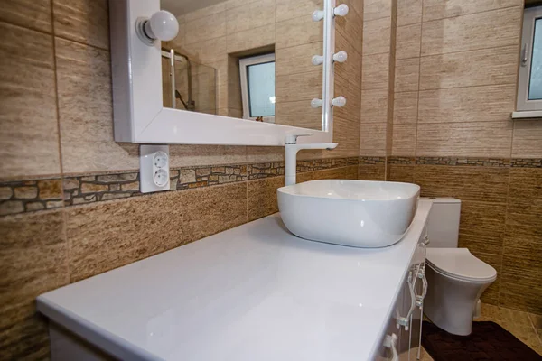 The interior of the bathroom with a big illuminated mirror, walk-in shower and elegant sink