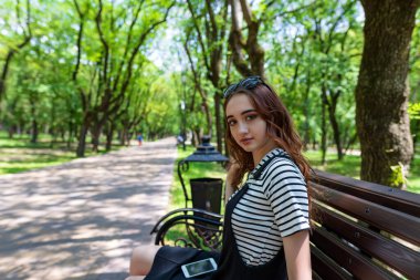 Çekici kızıl saçlı kız parkta bir bankta oturuyor ve cep telefonuyla konuşuyor.