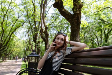 Çekici kızıl saçlı kız parkta bir bankta oturuyor ve cep telefonuyla konuşuyor.