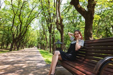 Çekici kızıl saçlı kız parkta bir bankta oturuyor ve cep telefonuyla konuşuyor.