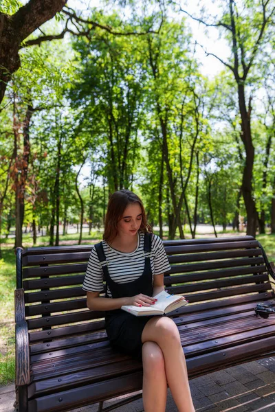 魅力的な赤毛ティーン女の子でザ パーク読書A本上のベンチと準備のための試験 — ストック写真