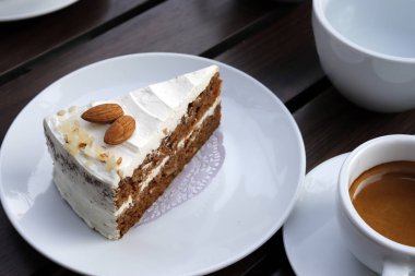 Bir fincan kahve, bir ahşap arka plan ile beyaz bir tabak içinde badem bir kek.