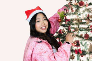 Fit young female athlete standing in front of a Christmas tree with gym equipment and gifts, celebrating the holiday season while showcasing fitness and strength.