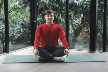 Young Asian man practicing yoga and meditation on a mat in nature.
