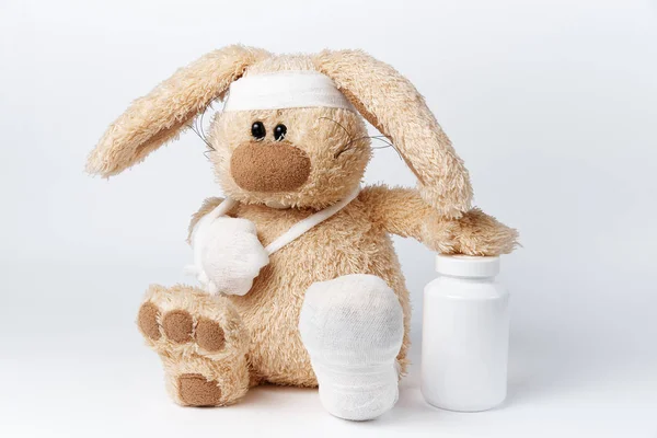 Cute sick bandaged hare with a jar of medicines on a white background.