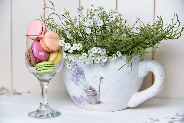 Bright colorful biscuits in a glass near a beautiful decorative vase with flowers.