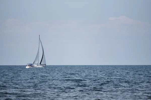 A view of the sea, a white yacht with sails and the sky.