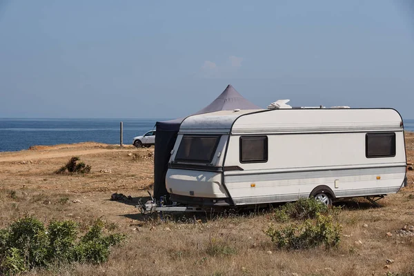 The house on wheels is parked on the beach in front of the blue sea in the wild