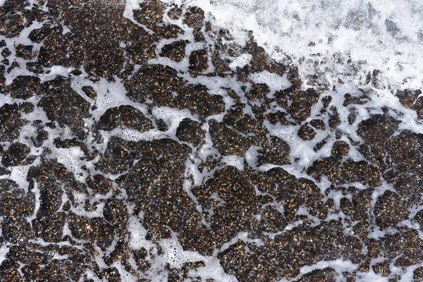 Background, texture sea water with foam and pebbles.