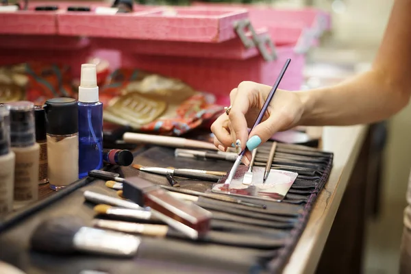 Hand makeup artist with brush for makeup close-up on the table with cosmetics.