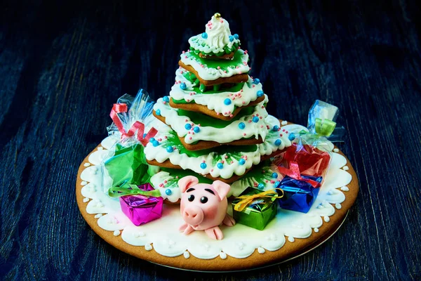Christmas gingerbread, sweet pig with gifts and sweets in the package under the Christmas tree on a dark wooden background.