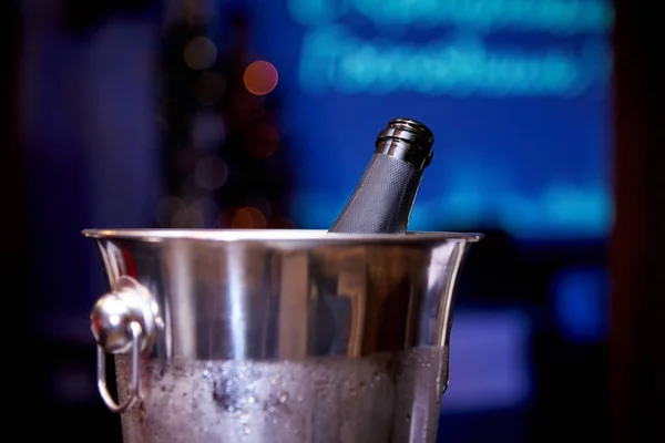 Open bottle of champagne in ice bucket on a dark blurred background with bokeh.