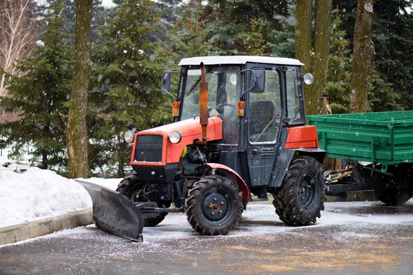 The municipal service of the city cleans the roads from the snow. Snow blower in the park on a winter day with falling snow.