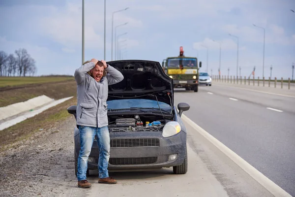 Nervous young man near broken car on the highway.