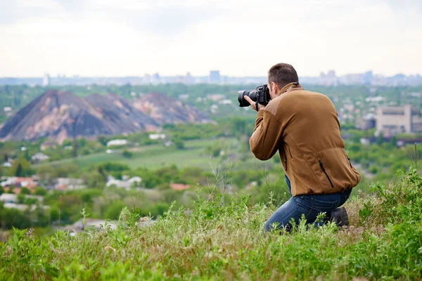 Photographer with a DSLR camera on a hill. A young man photographs the landscape on DSLR camera.