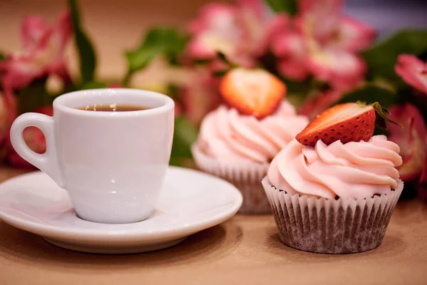 Chocolate cupcakes with strawberries. Cupcakes and a cup of coffee on the table with flowers. Selective focus.